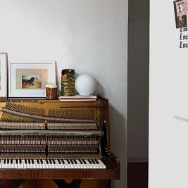 Detail of a white-walled room with a piano, featuring Ceramic Pot Candles in platinum glaze elegantly placed on top, adding a touch of artisanal sophistication to the decor.