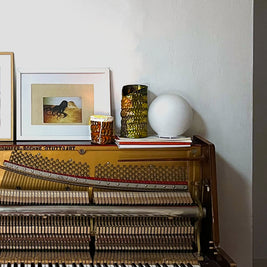 Close-up of Ceramic Pot Candles in platinum glaze displayed on a piano in a white-walled room, highlighting their intricate texture and artisanal craftsmanship.
