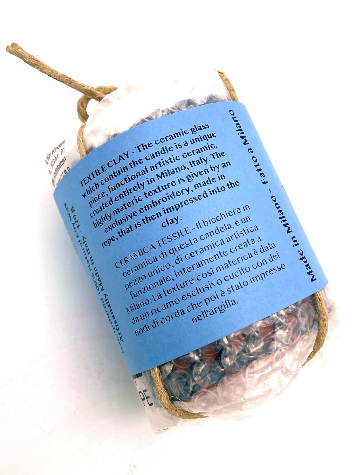Back view of the Ceramic Pot Candle packaging, with a label describing the textile ceramic process, where the material texture is created by pressing exclusive knotted cord embroidery into clay.