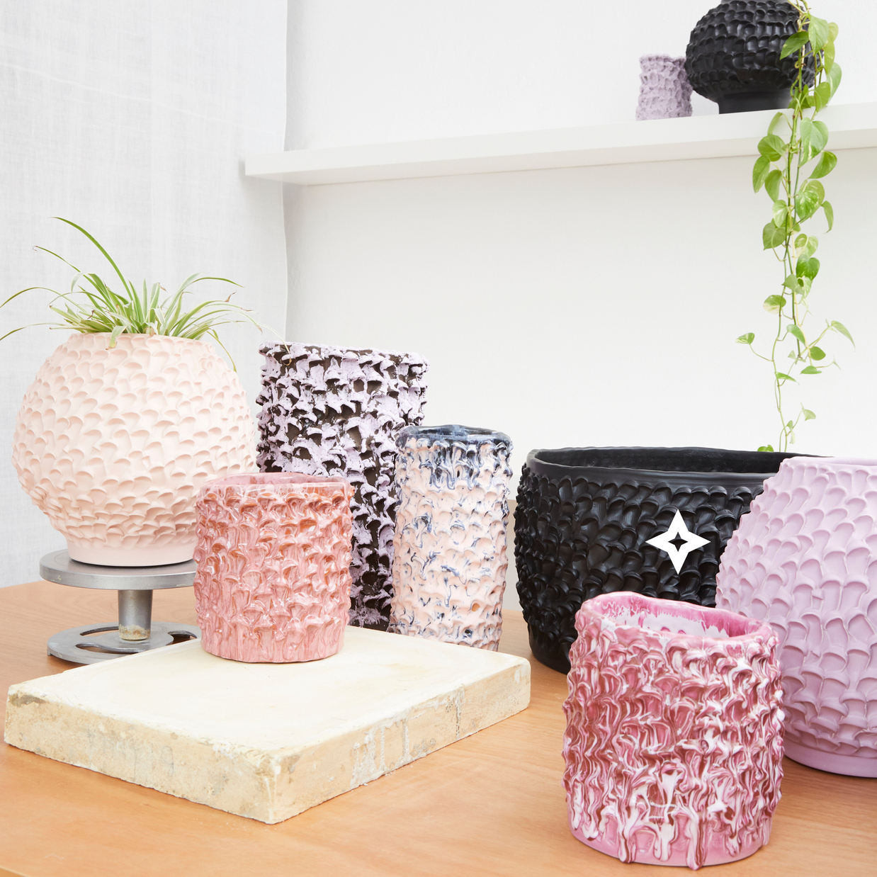 Composition of 9 Ceramic Vases in Candy Violet, Lilac, and White, displayed on white shelves with plants, in a minimalist setting featuring light wood surfaces and a white wall.