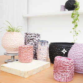 Composition of 9 Ceramic Vases in Candy Violet, Lilac, and White, displayed on white shelves with plants, in a minimalist setting featuring light wood surfaces and a white wall.
