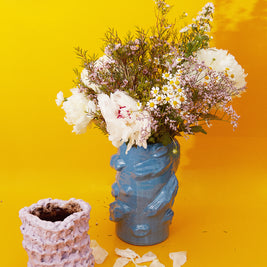 Artistic composition featuring the Ceramic Vase in Lilac Bubble & Chocolate alongside a blue vase with plants, set against a vibrant yellow backdrop.