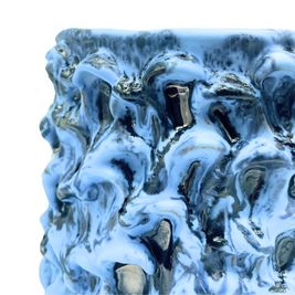 Close-up detail of the Ceramic Vase in Whispy Matte Blue and Liquid Bronze, emphasizing its textured surface with delicate silvery and bronze splashes on a light blue surface.