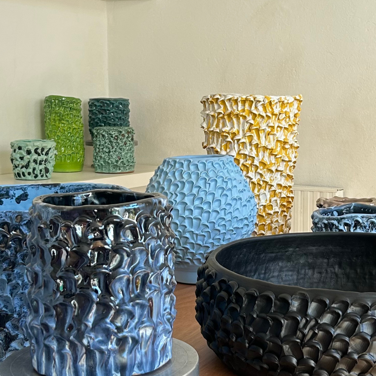 Arrangement of multiple vases from the Onda Series on a light wood table with a creamy background, utilizing a small shelf to create varying heights for an elegant display.
