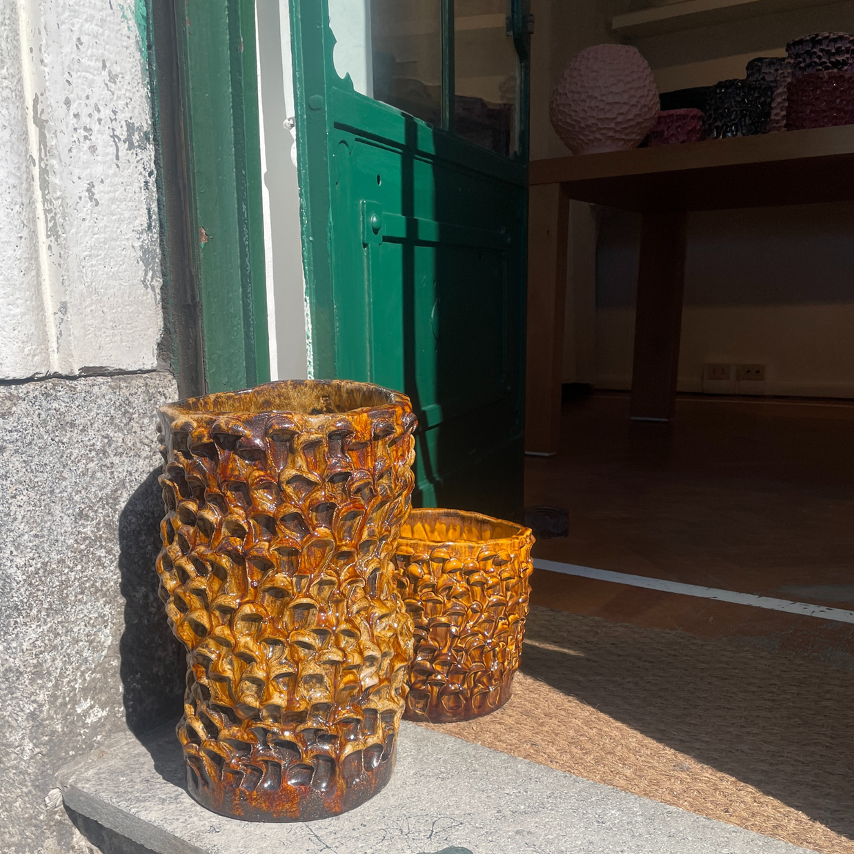 Two Ceramic Vases in Translucent Honey displayed outdoors on a concrete step, with one vase placed in front of an open door, blending seamlessly with the natural light.