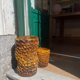 Two Ceramic Vases in Translucent Honey displayed outdoors on a concrete step, with one vase placed in front of an open door, blending seamlessly with the natural light.