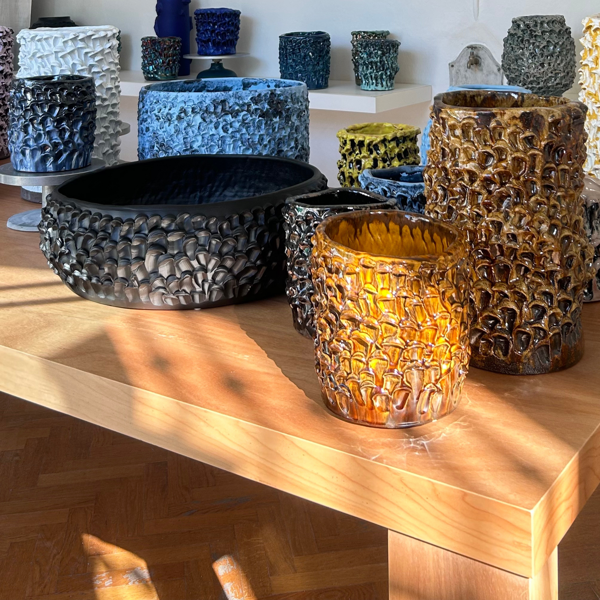 Multiple Ceramic Vases in Translucent Honey from the Onda Series arranged on a light wood table, creating an elegant and cohesive display of unique hand-crafted pieces at different heights.