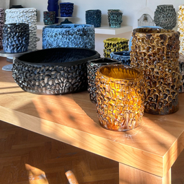 Multiple Ceramic Vases in Translucent Honey from the Onda Series arranged on a light wood table, creating an elegant and cohesive display of unique hand-crafted pieces at different heights.
